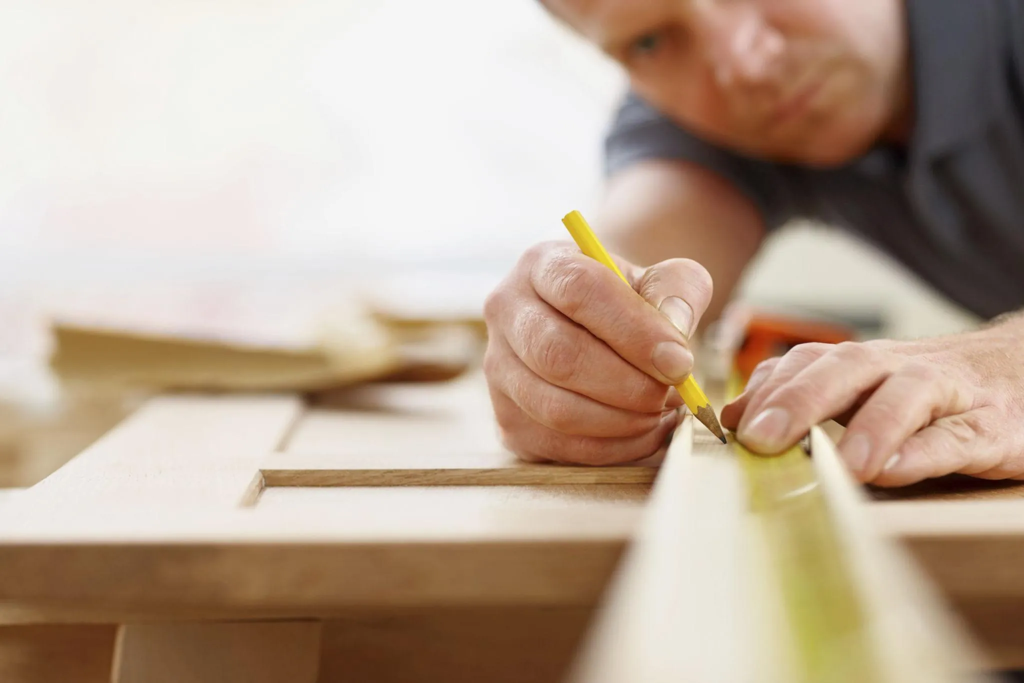Joiner marking a precise measurement on timber with a pencil and square